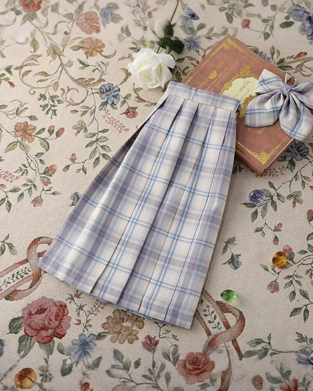 A JK Plaid Skirt, featuring a pleated design, rests on a floral patterned surface.