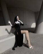 A woman wearing a black Anime Nun Costume - Halloween Edition, complete with gloves and a cross.