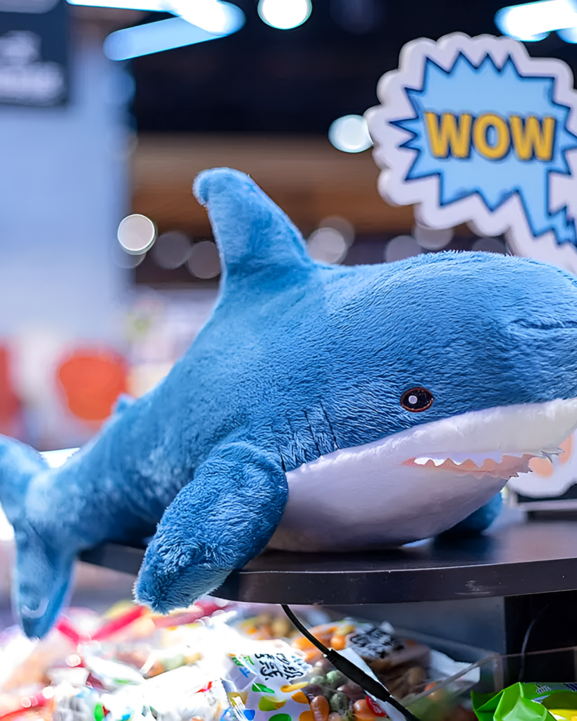 Blue shark plushie, Alfred the Shark, displayed on a wooden table.