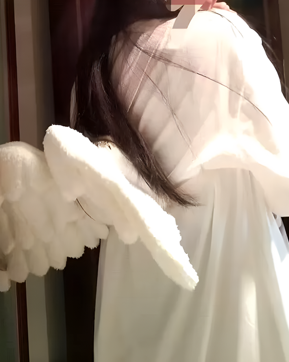 White angel wing backpack attached to a white dress, showing the plush details.