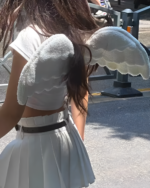 Woman wearing an angel wing backpack, white plush wings, outdoor setting.