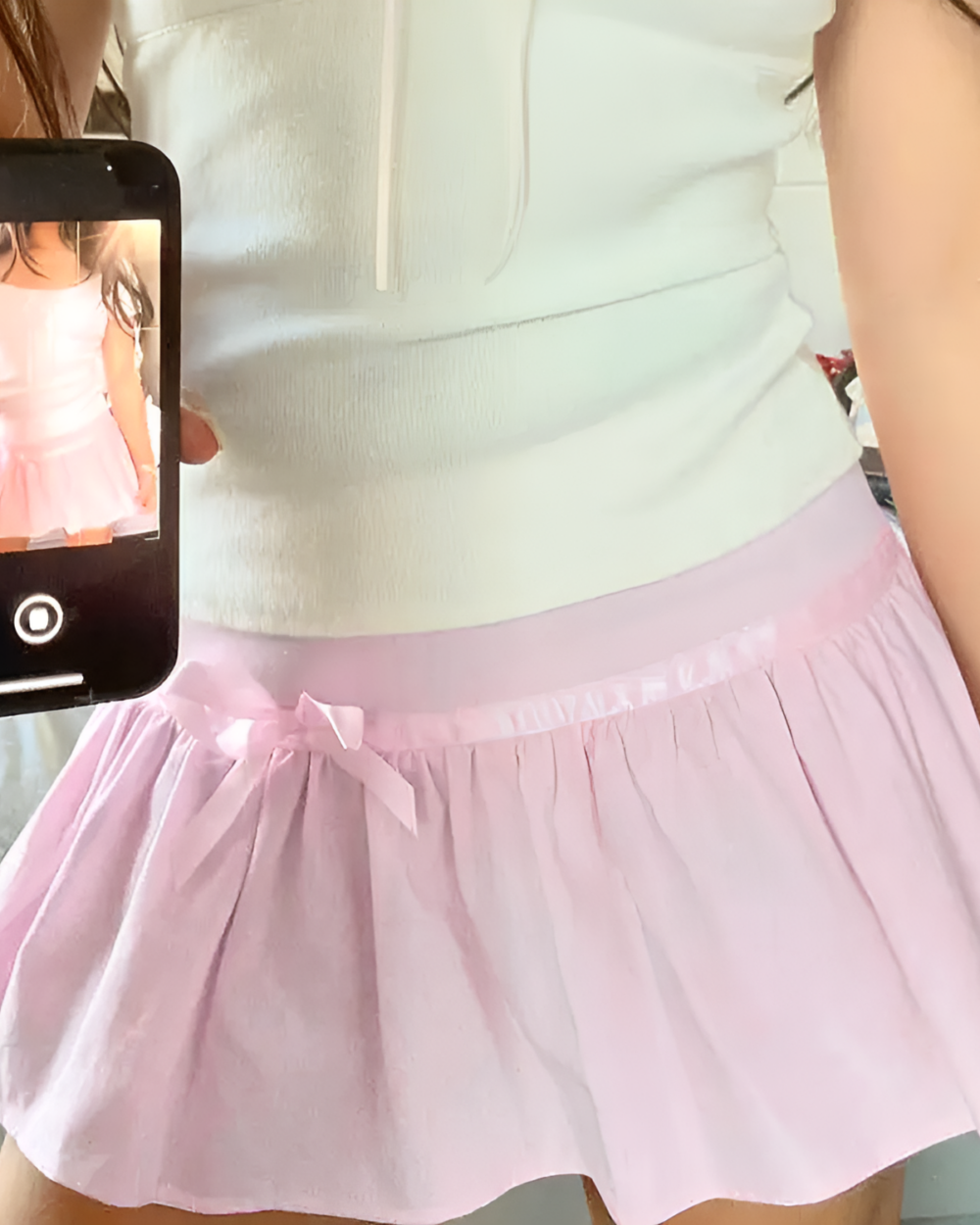 Pink mini skirt with pleats and bow, part of the coquette aesthetic.