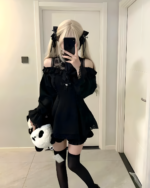 Woman modeling a black Bowed Mini Dress, a Gothic Lolita dress, with black stockings and a blonde wig.