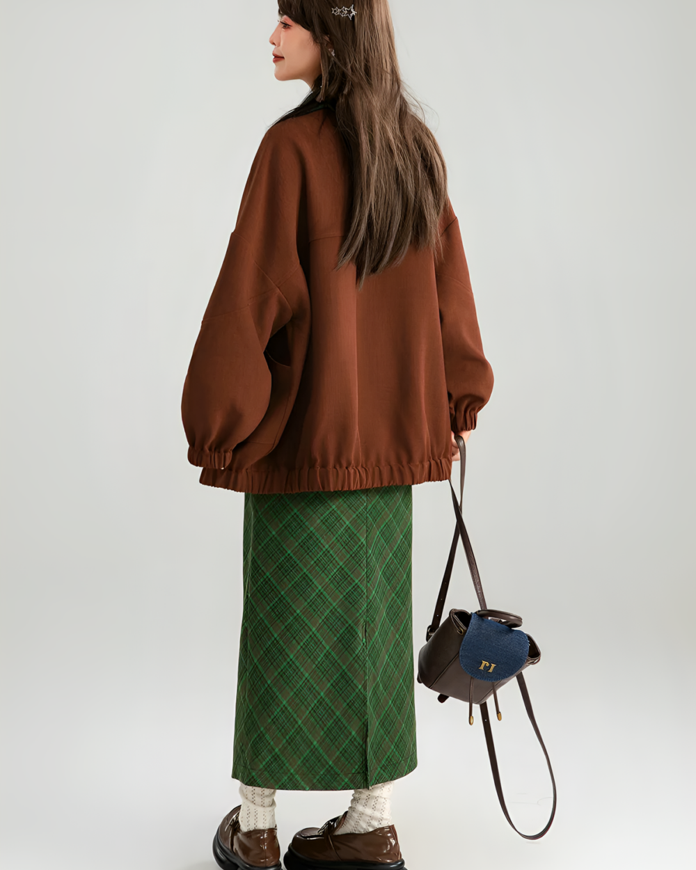 Woman wearing a brown corduroy jacket with a plaid skirt and bag.