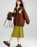 Woman wearing a brown corduroy jacket layered over a green outfit, with a small bag.
