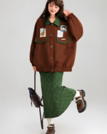 Model wearing a brown corduroy jacket with patches and a green plaid skirt.