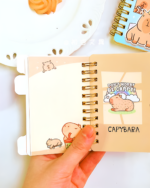 Close-up of a spiral-bound Capybara Notebook featuring illustrations and text.
