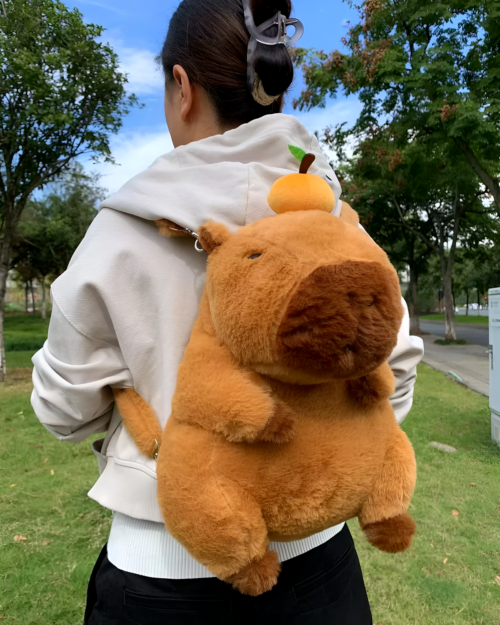 Person wearing a beige hoodie with a brown Capybara Plushie backpack featuring a fruit detail.
