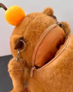 Close-up of a brown Capybara Plushie backpack with an open zipper and a carrot detail on top.