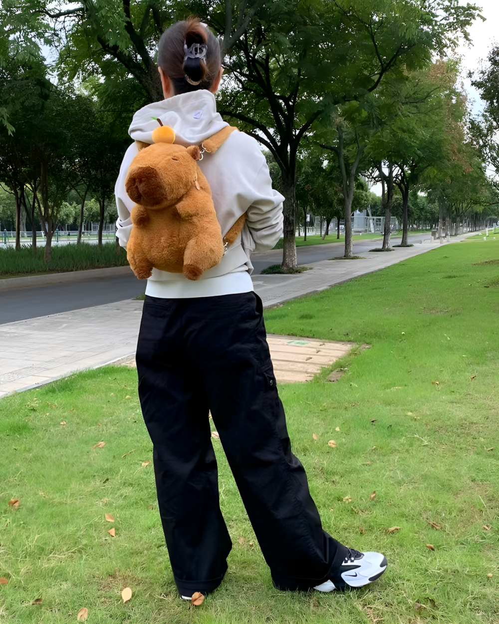 Woman wearing a Capybara Plushie backpack outdoors. The plushie is brown and resembles a capybara.