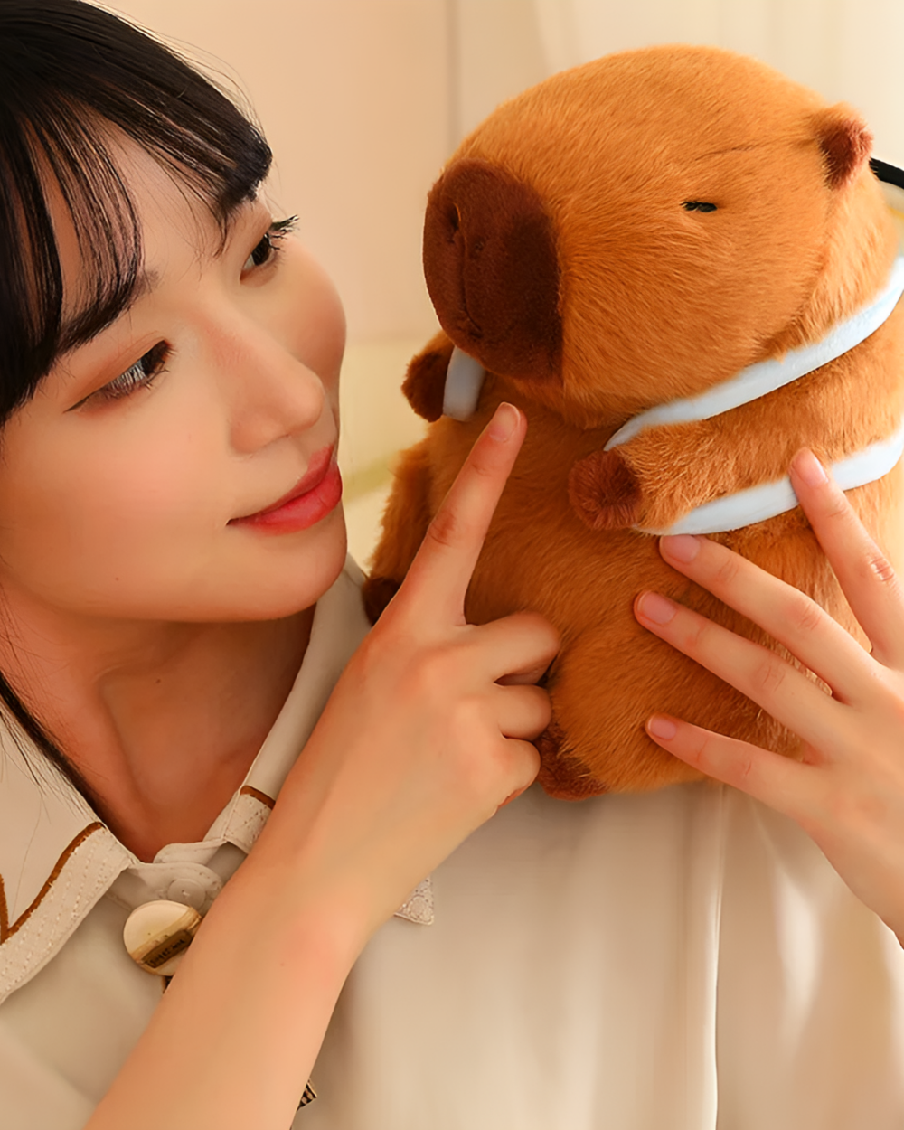 Woman interacting with a brown capybara plushie wearing a light blue scarf. The Nature Explorer Edition plush is soft and detailed.