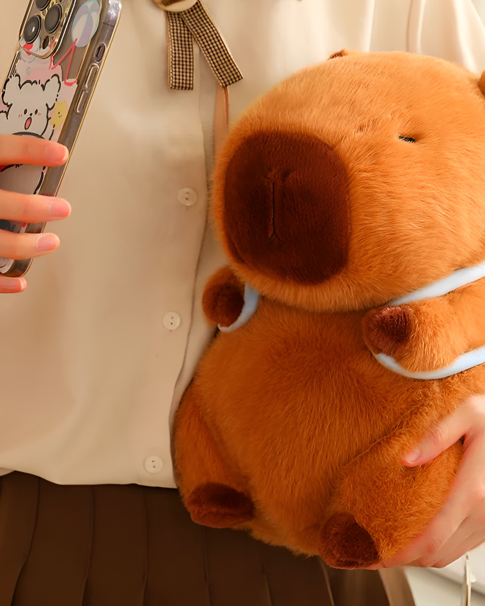Close-up of a brown capybara plushie held by a person, with a phone in the background.