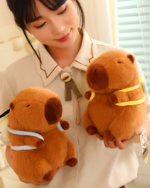 A woman holding two brown capybara plushies with yellow scarves. These cute capybara plushie toys are soft and cuddly.