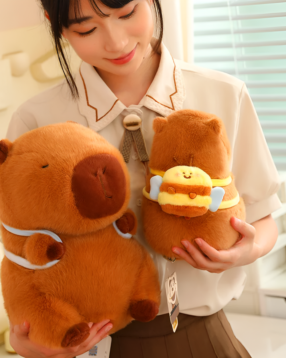 Woman holding two brown capybara plushies from the Nature Explorer Edition. A cute capybara plushie in a bee costume is also visible.
