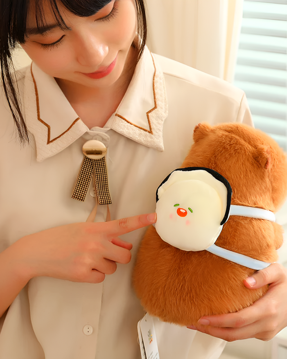 A woman points to a cute capybara plushie with a small animal toy on its back. Perfect for nature lovers.
