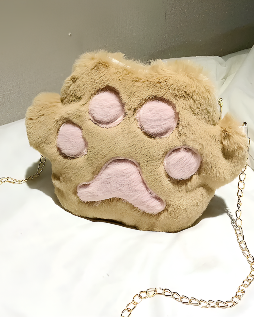 Close-up of a tan cat paw purse with a chain strap and pink lining.
