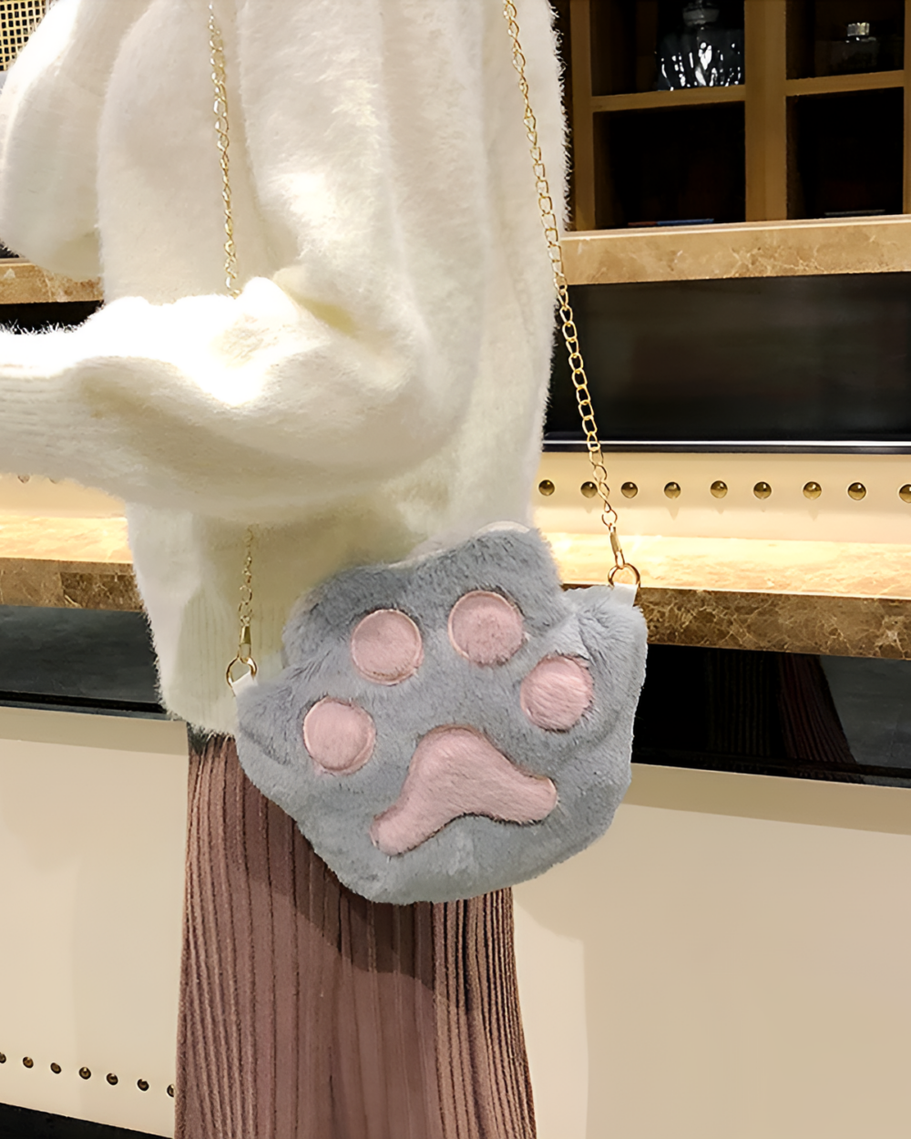 Close-up of a gray and white cat paw purse with a gold chain strap.