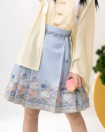 Girl wearing a light blue celestial pleated skirt with a floral pattern and a cream-colored jacket.