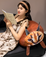 A Chonky Big Floppa plushie is resting on a couch with a person reading a book.