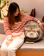 A woman holding a Chonky Realistic Palla's cat plush on a couch.
