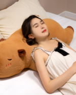 Woman sleeping with a large, brown capybara plushie. Soft toy used as a pillow.
