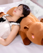 Woman sleeping with a large, brown capybara plushie. Soft toy for cuddling and comfort.