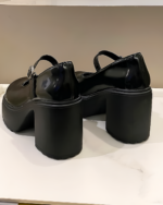Black Chunky Mary Janes with a thick platform heel and ankle buckle, displayed on a white surface.