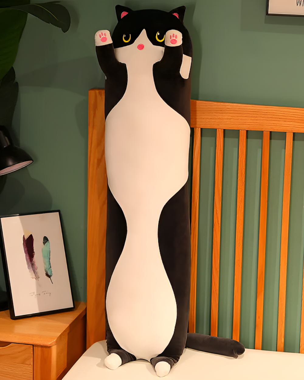Black and white long cat plush pillow leaning against a headboard. Ideal snuggle companion.