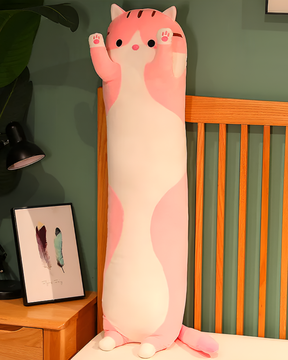 Pink and white long cat plush pillow, the Cloud Kitty Long Snuggle Pillow, shown on a bed.