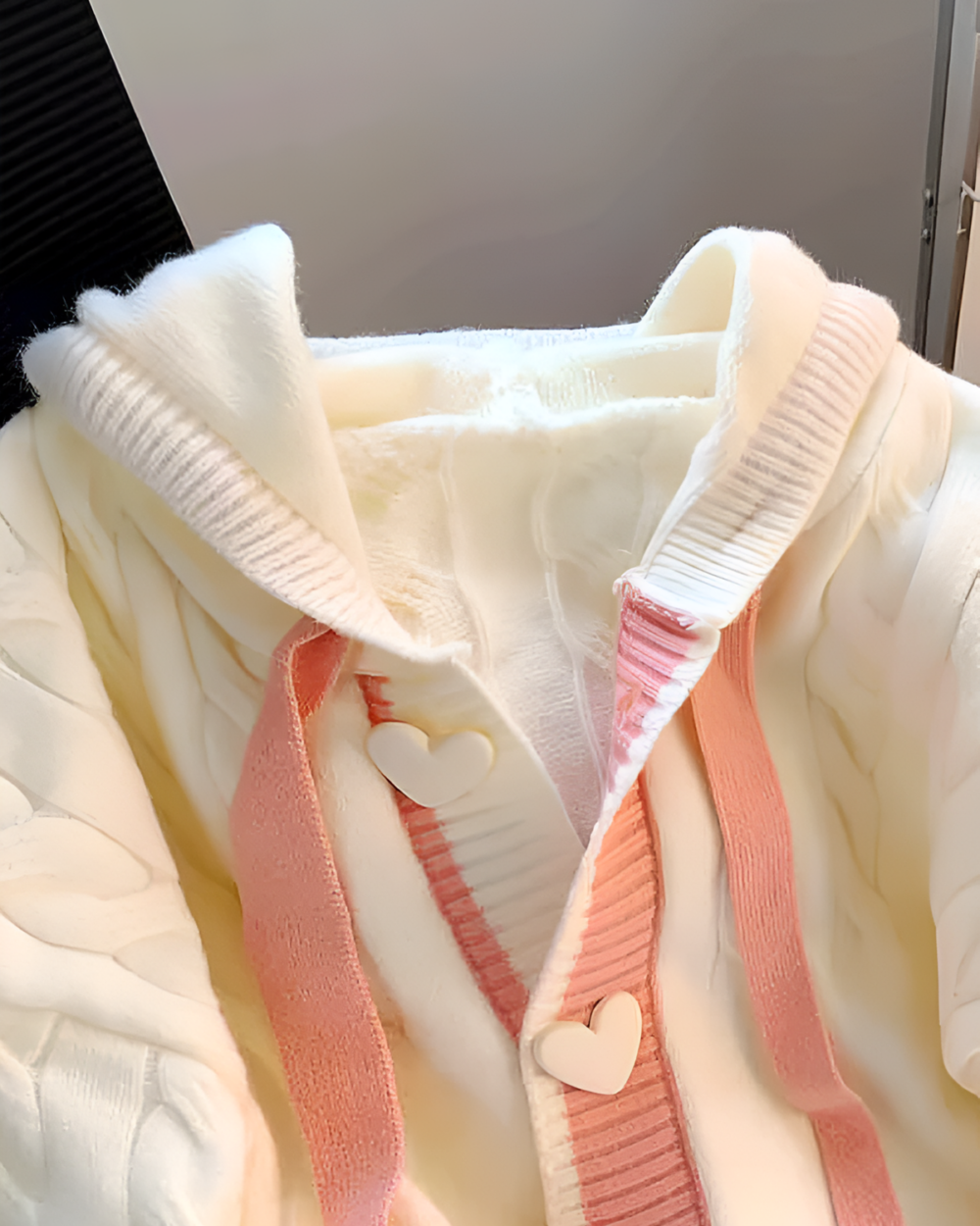 Creamy pink knit sweater close-up showing details, including a hood and buttons.