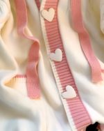 Creamy pink knit sweater with heart-shaped buttons on the front.