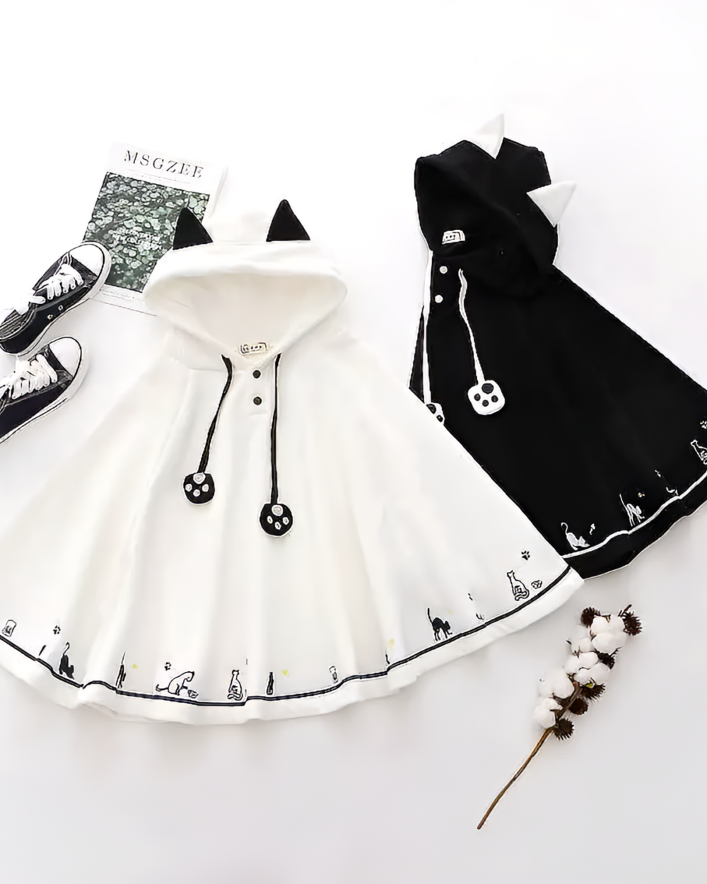 Crescent Neko-Ear Hooded Poncho product photo 1 White and black Crescent Neko-Ear Hooded Poncho laid flat with shoes and flowers. A cute neko ear poncho option.