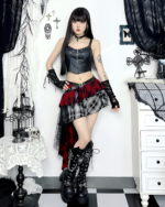Model wearing a crimson and black pleated goth punk skirt with a black top and boots. A full-length shot.
