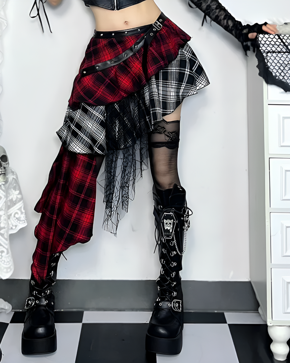 Model wearing a crimson and black pleated goth punk skirt with black boots and fishnet stockings. Asymmetric design with plaid pattern.