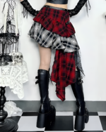 Model wearing a crimson and black pleated goth punk skirt with knee-high boots. The skirt features a layered, asymmetrical plaid design.