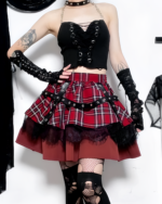 A model wearing a Crimson Strap Lace Mini Skirt, a goth punk skirt with a plaid pattern and black lace trim. Includes a studded belt.