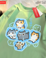 Close-up of a green cutecore cat shirt featuring an ice cube cat graphic. The tee has a tag attached.