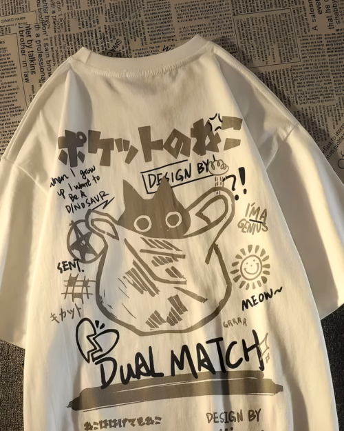 Close-up of a white Dual Match Neko Bag T-Shirt featuring a cartoon cat and text design. The shirt has a playful, illustrated aesthetic.