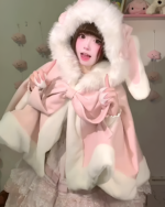 Woman wearing a pink Fluffy Bunny Hooded Cloak with white faux fur trim, posing indoors.