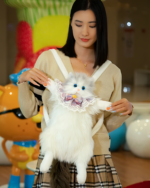 Woman holding a fluffy white cat backpack, the Fluffy Chonker Bag, featuring a bow and embellishments.
