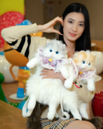Woman holding two fluffy cute cat backpacks (Fluffy Chonker Bag) plush toys.