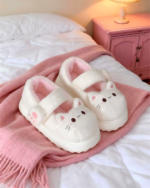 Fluffy Mary Jane slippers resting on a pink blanket near a bed.