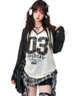 Model wearing a white graphic tee and a black and grey gothic pleated skirt. Styled with headphones and a jacket.