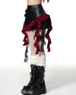 Model wearing a black and red gothic pleated skirt with lace and plaid details, paired with boots.