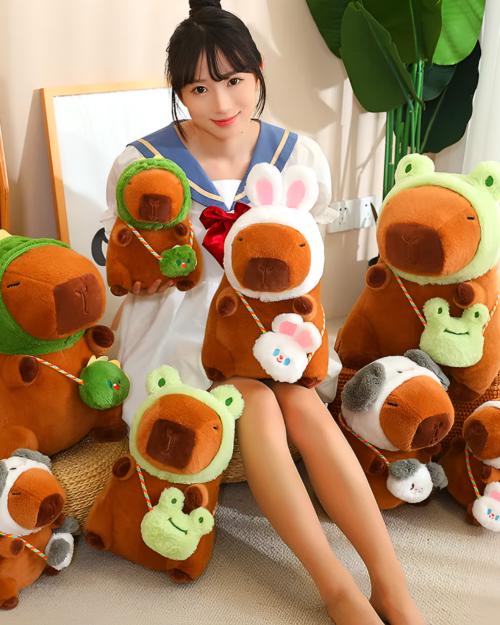 A person holding multiple hatted capybara plushies, some designed as squeaky purses. Includes different colors and hat styles of the capybara plushie.