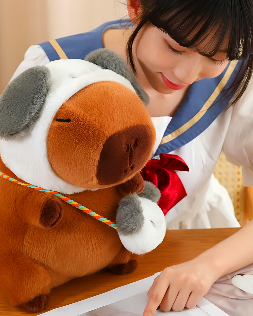 Woman holding a brown capybara plushie with a hat. This squeaky purse edition capybara plushie is detailed and soft.