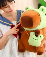 A person holding a brown capybara plushie with a green hat and a small matching capybara plushie accessory. This is the Hatted Capybara Plushies - Squeaky Purse Edition.