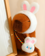 Hatted capybara plushie with a bunny hat and strap, designed as a squeaky purse. Features a cute face and soft fur.