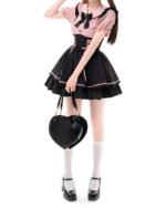 Model wearing a pink and black Heartache Lace-Up Pinafore Coord, a Jirai Kei outfit with a heart-shaped bag and Mary Jane shoes.