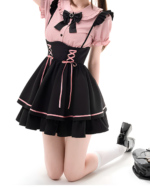 Model wearing a pink and black Jirai Kei outfit with lace details and a pinafore style. Includes a ruffled collar and lace-up accents.